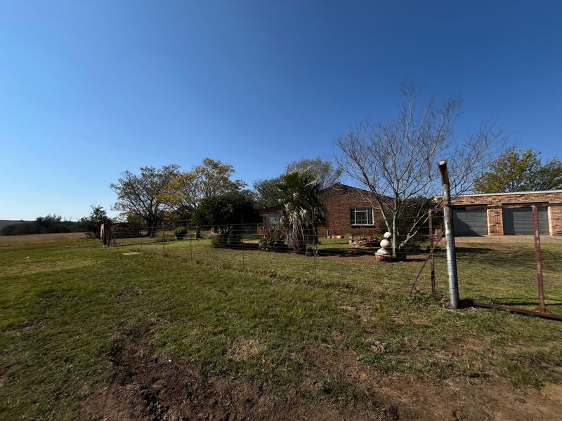 Front view of a brick farm house featuring a double garage, wire fencing, and surrounding open land.