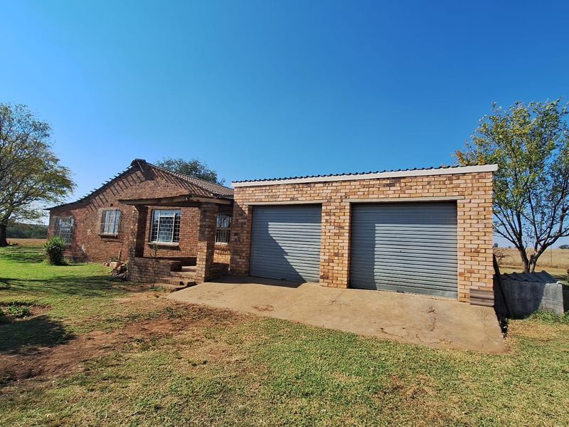 A single-story face brick farmhouse featuring a double garage with roller shutter doors and a covered front entrance, set on a spacious rural plot.