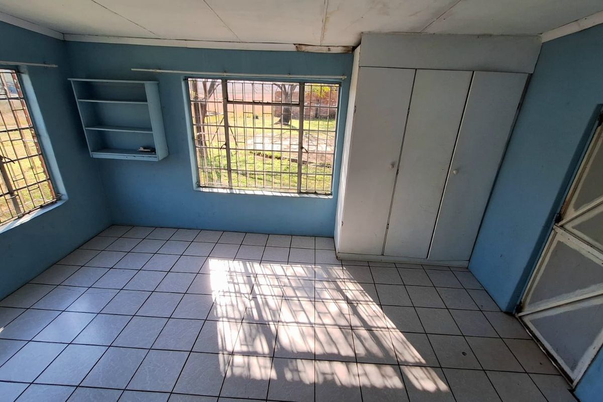 An empty bedroom featuring tiled flooring, built-in cupboards, and security bars on the windows, requiring some cosmetic maintenance and ceiling repairs.