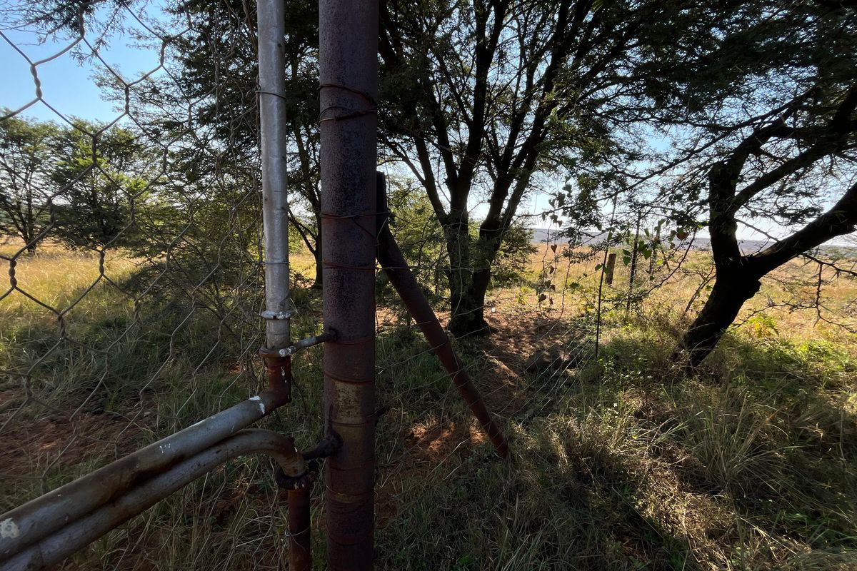 A view of the farm perimeter featuring wire mesh fencing supported by weathered and corroded metal posts set against a natural landscape.