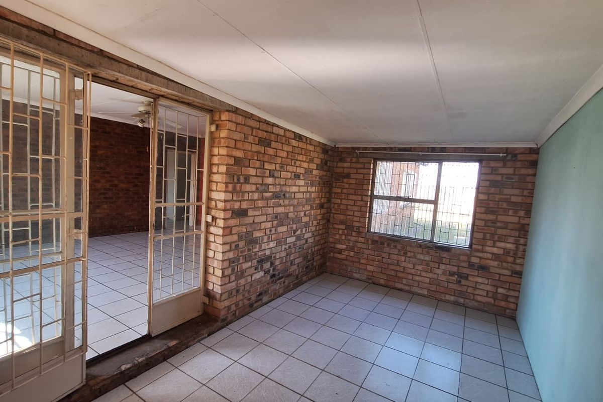 An empty living area featuring exposed brick walls, tiled flooring, and security gates, offering a blank canvas for renovation and interior design updates.