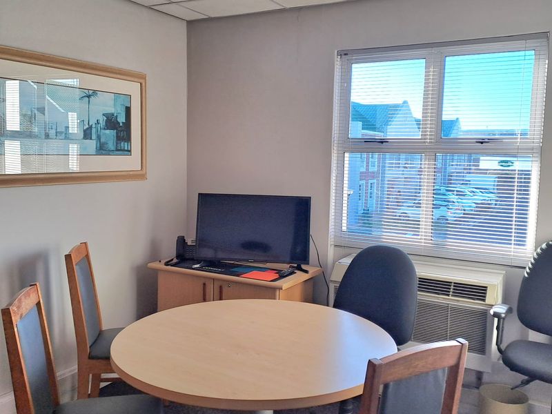 A functional office space featuring a suspended ceiling, window blinds, and a built-in HVAC unit, suitable for a small meeting or workspace.