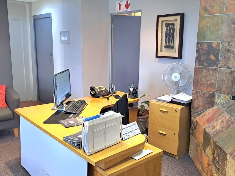 A functional office space featuring a stone-clad fireplace, recessed ceiling lighting, and carpeted flooring, suitable for a professional work environment.