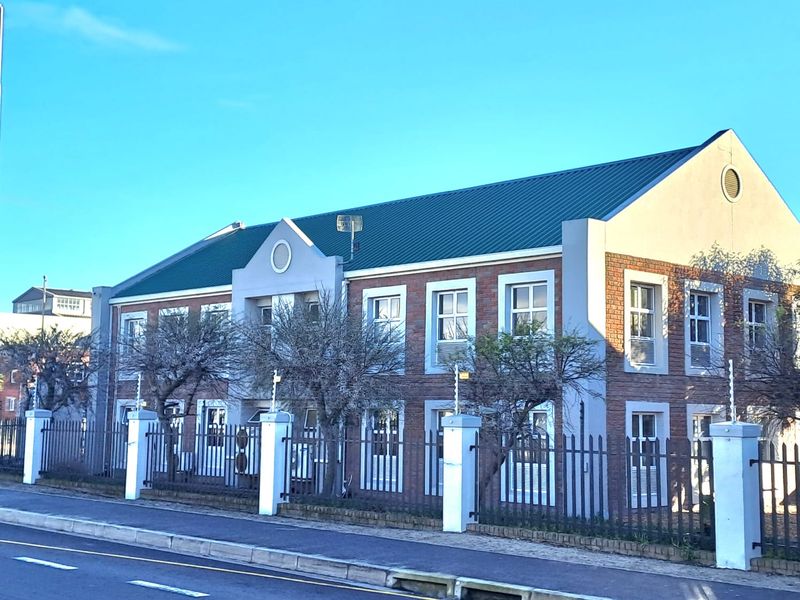 Front exterior view of a two-story brick office building featuring a metal roof and secure perimeter fencing.