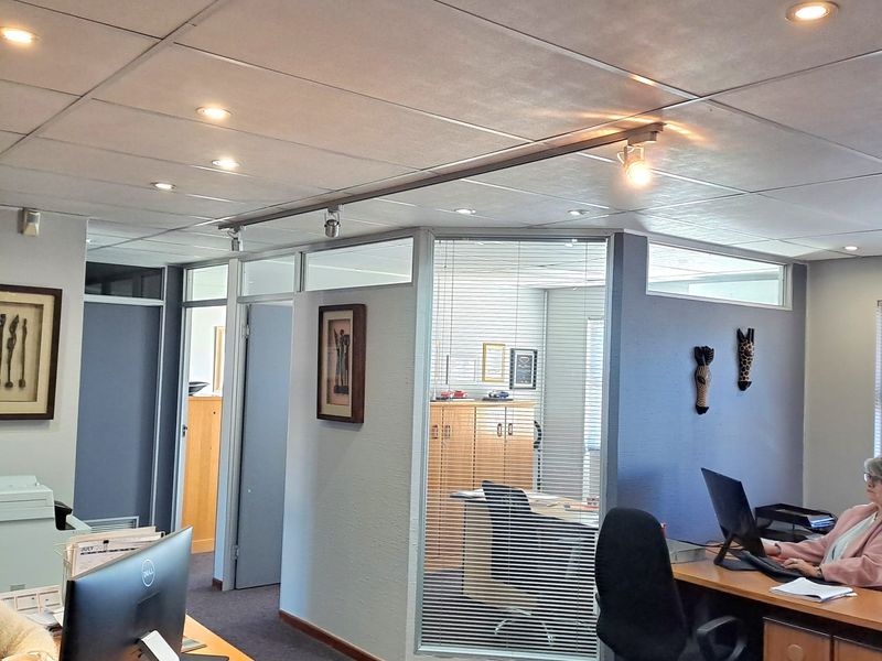 A professional office space featuring glass partitions, suspended ceilings with integrated lighting, and carpeted flooring, providing a functional and well-lit work environment.