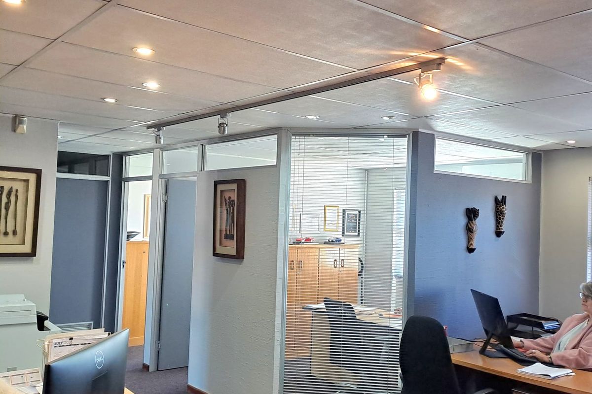A professional office space featuring glass partitions, suspended ceilings with integrated lighting, and carpeted flooring, providing a functional and well-lit work environment.