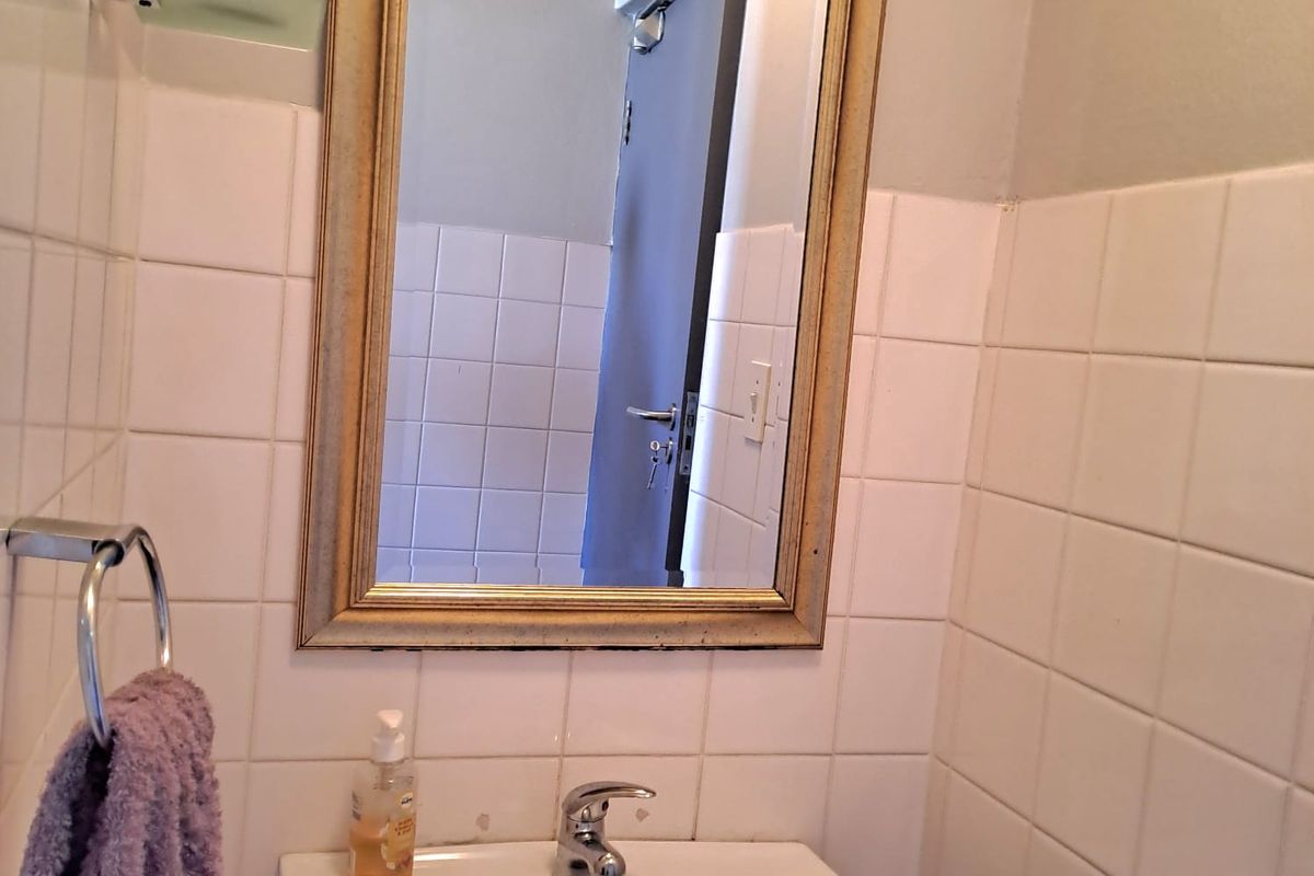 A functional office bathroom featuring a wall-mounted basin, chrome mixer tap, and tiled splashback with a decorative wall mirror.
