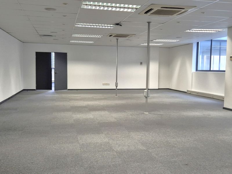A spacious, open-plan office area featuring carpeted flooring, a suspended ceiling with integrated lighting, and ducted air conditioning.