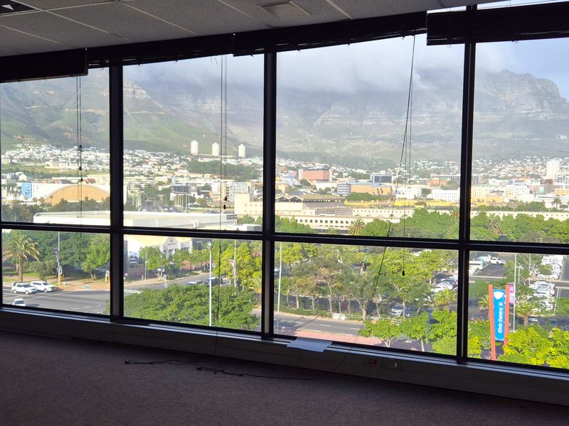 Spacious empty office area featuring expansive floor-to-ceiling windows with panoramic mountain and city views.