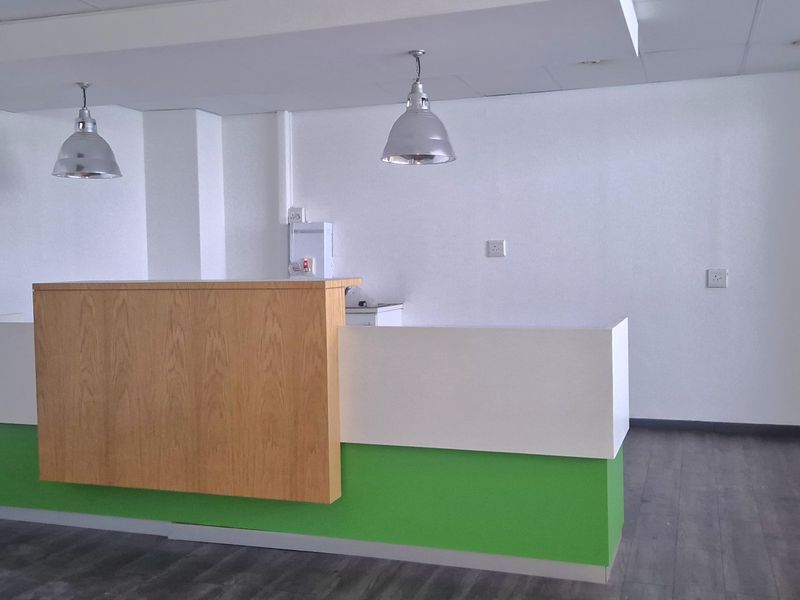 A bright, open-plan office space featuring a modern built-in reception desk, pendant lighting, and durable laminate flooring.