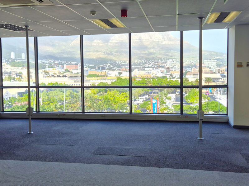 Spacious open-plan office area featuring large floor-to-ceiling windows with panoramic city and mountain views, suspended ceilings, and carpeted flooring.