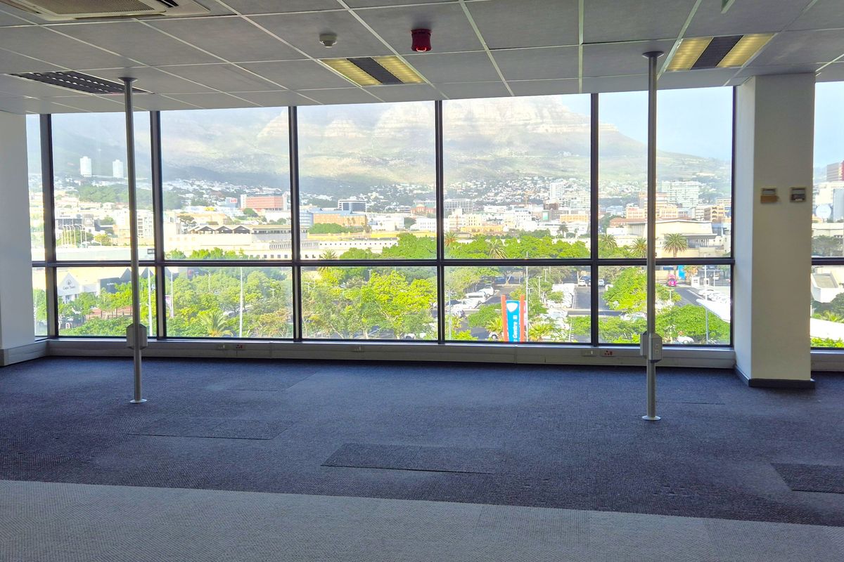 Spacious open-plan office area featuring large floor-to-ceiling windows with panoramic city and mountain views, suspended ceilings, and carpeted flooring.