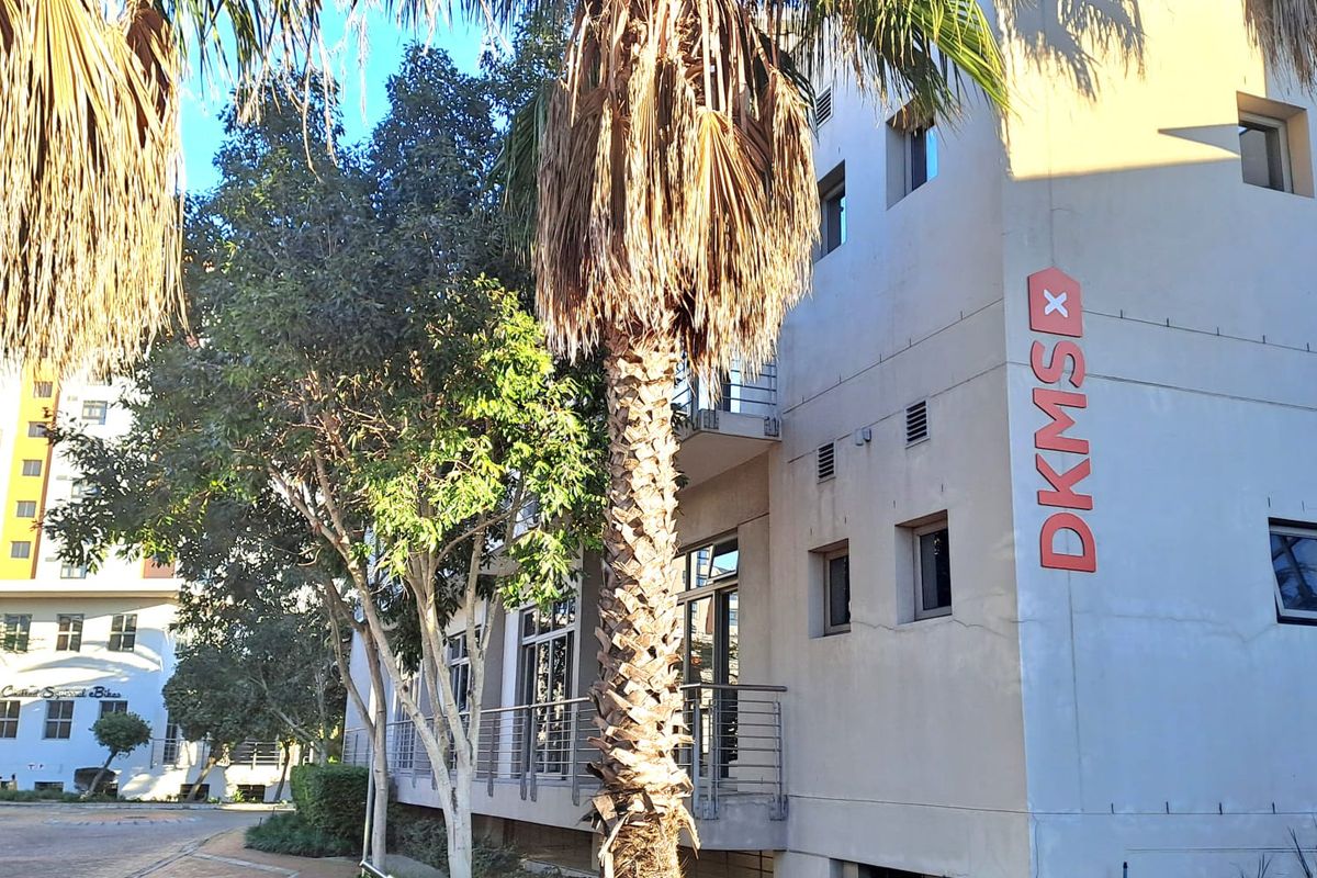 Exterior view of a multi-story office building featuring a prominent vertical sign, paved walkways, and established landscaping.