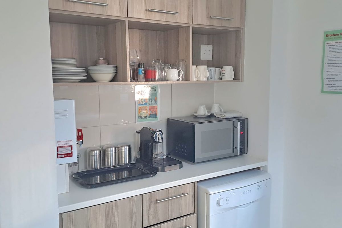 A compact office kitchenette featuring light wood-grain cabinetry, a white countertop, tiled backsplash, and an integrated dishwasher.