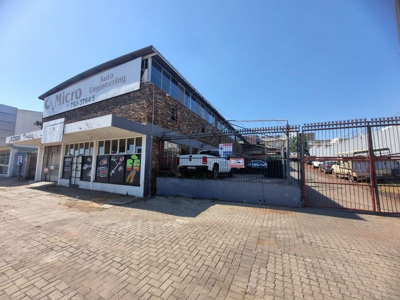 Front exterior view of a commercial auto engineering property featuring brick facade, secure perimeter fencing with razor wire, and gated driveway access.