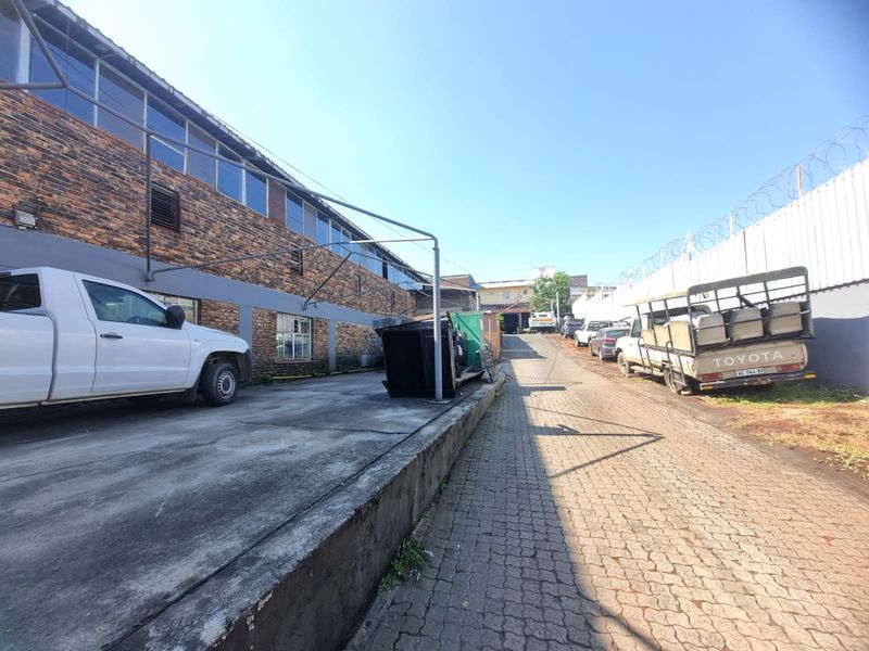 Rear exterior view of a commercial property featuring a brick facade, paved driveway, and secure perimeter fencing with razor wire.