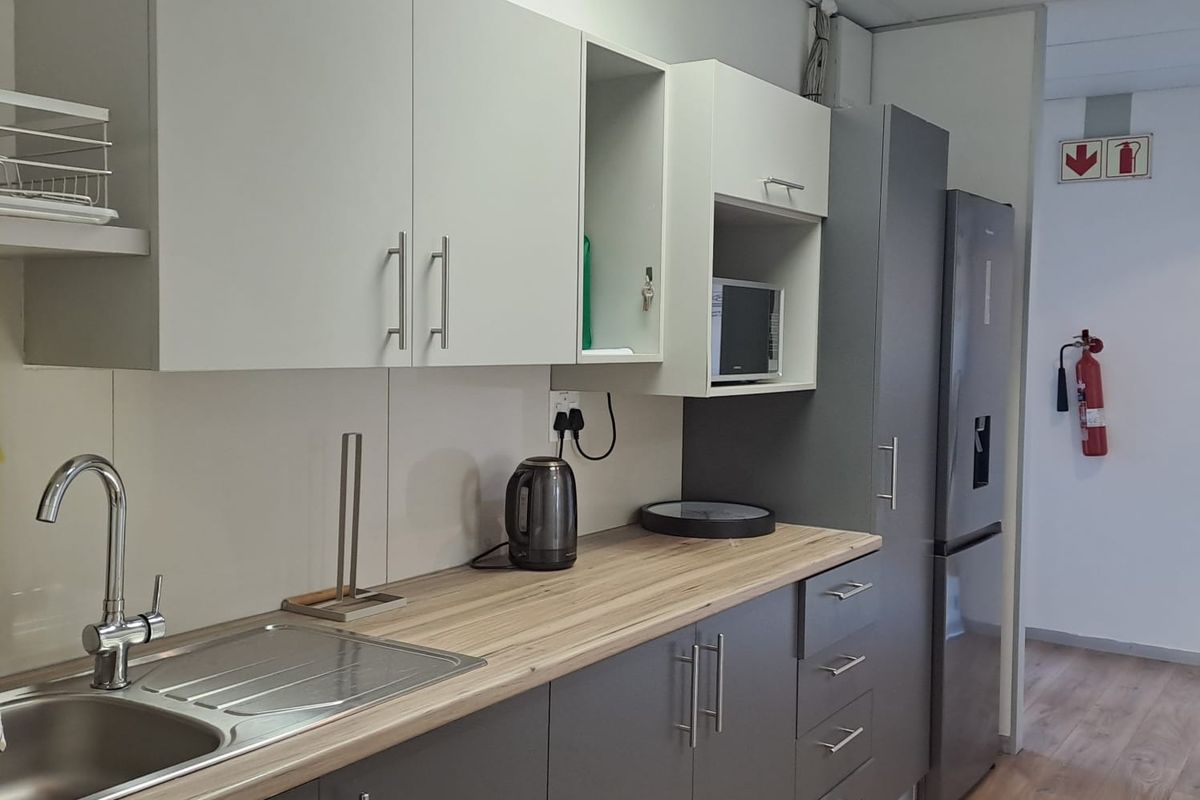 A modern office kitchenette featuring grey cabinetry, wood-look countertops, a stainless steel sink, and integrated storage space.