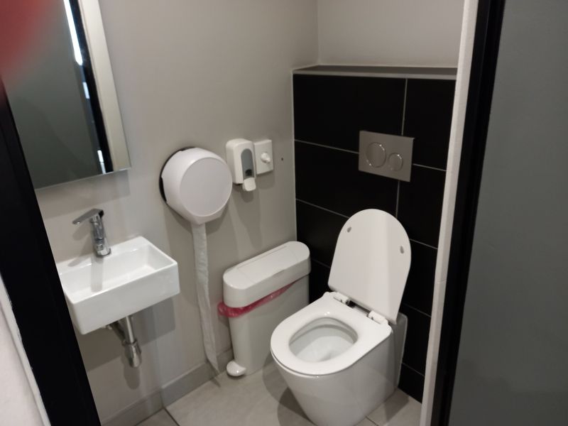 A modern, compact office restroom featuring a wall-hung toilet with a concealed cistern, a wall-mounted basin, and contemporary black tiled accents.