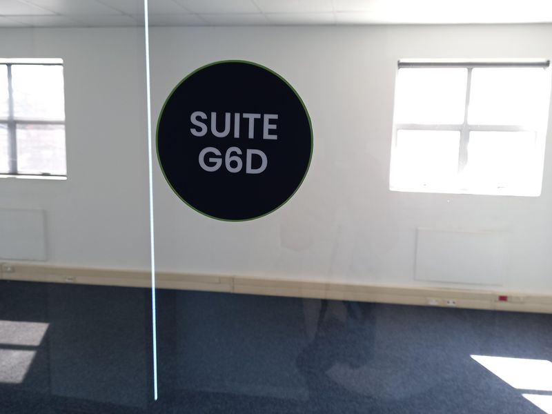 An empty office suite featuring carpeted flooring, a suspended ceiling, and a glass partition wall with suite signage.