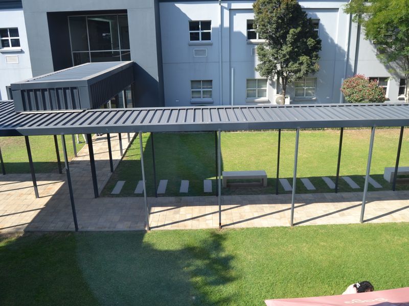 An elevated view of a modern office exterior featuring a covered walkway, paved pathways, and well-maintained landscaped lawn areas with fixed seating.