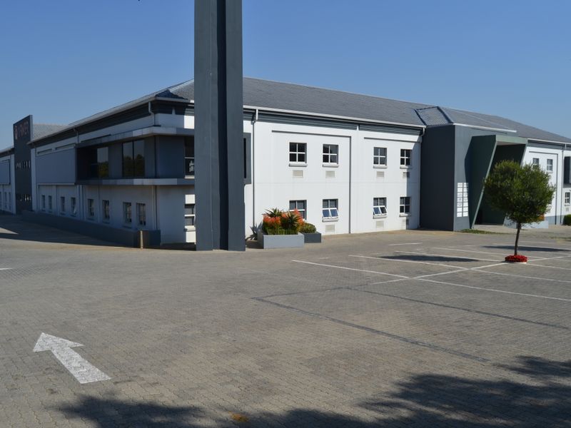 Exterior view of a modern multi-story office building featuring a paved parking area and a clean, professional facade.