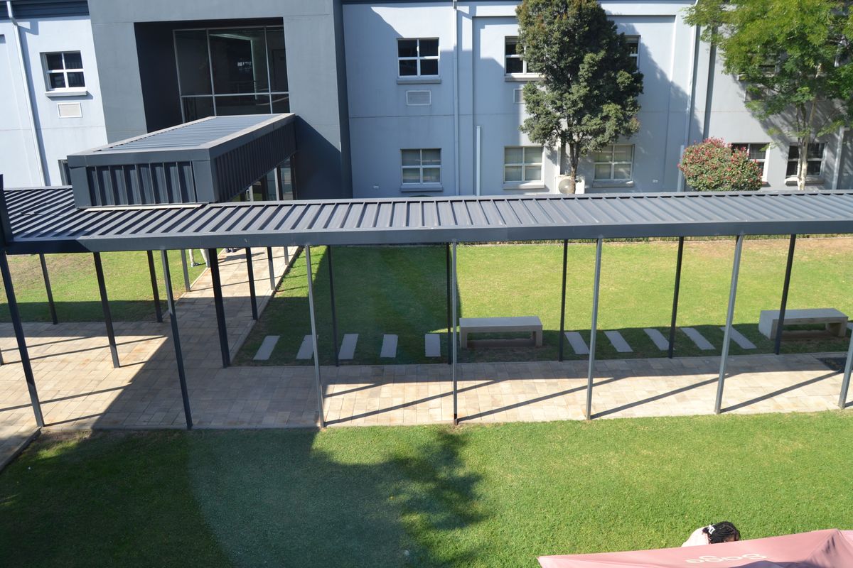 An elevated view of a modern office exterior featuring a covered walkway, paved pathways, and well-maintained landscaped lawn areas with fixed seating.