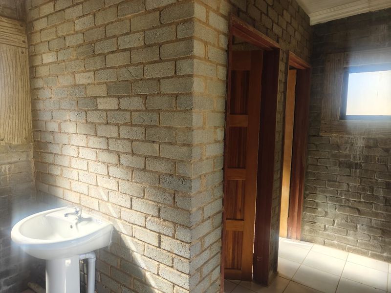 A bathroom space featuring exposed brick walls, tiled flooring, and a pedestal basin, currently in an unfinished state.