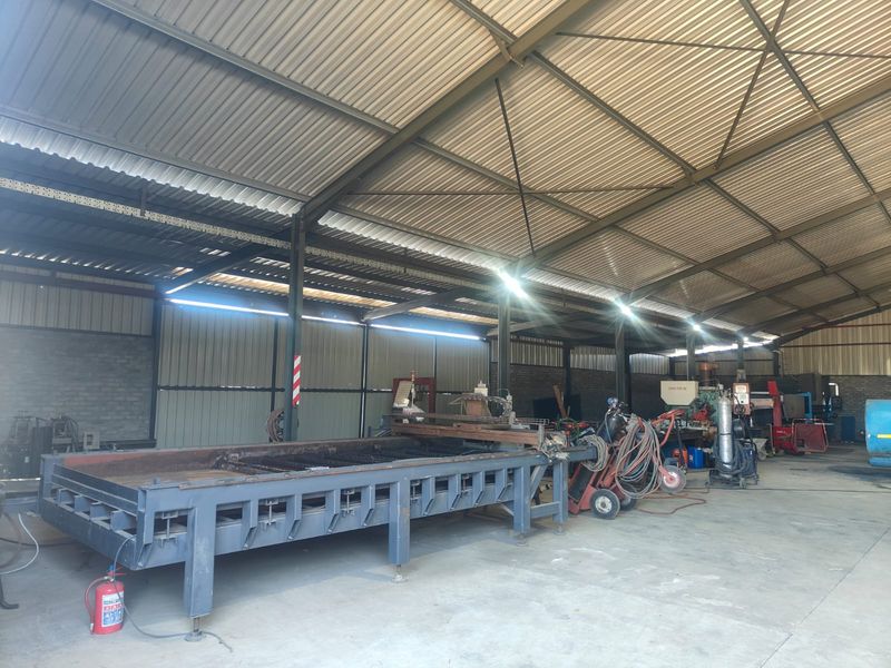 Large industrial workshop or utility space featuring a steel portal frame structure, corrugated metal roofing, and durable concrete flooring.
