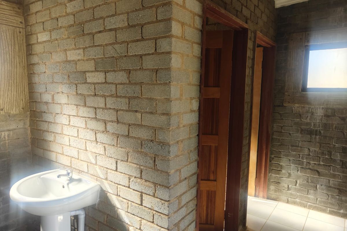 A bathroom space featuring exposed brick walls, tiled flooring, and a pedestal basin, currently in an unfinished state.
