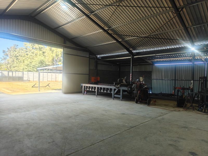 Spacious industrial utility shed featuring a high-clearance corrugated metal roof, concrete flooring, and large sliding access doors, suitable for workshop or storage use.