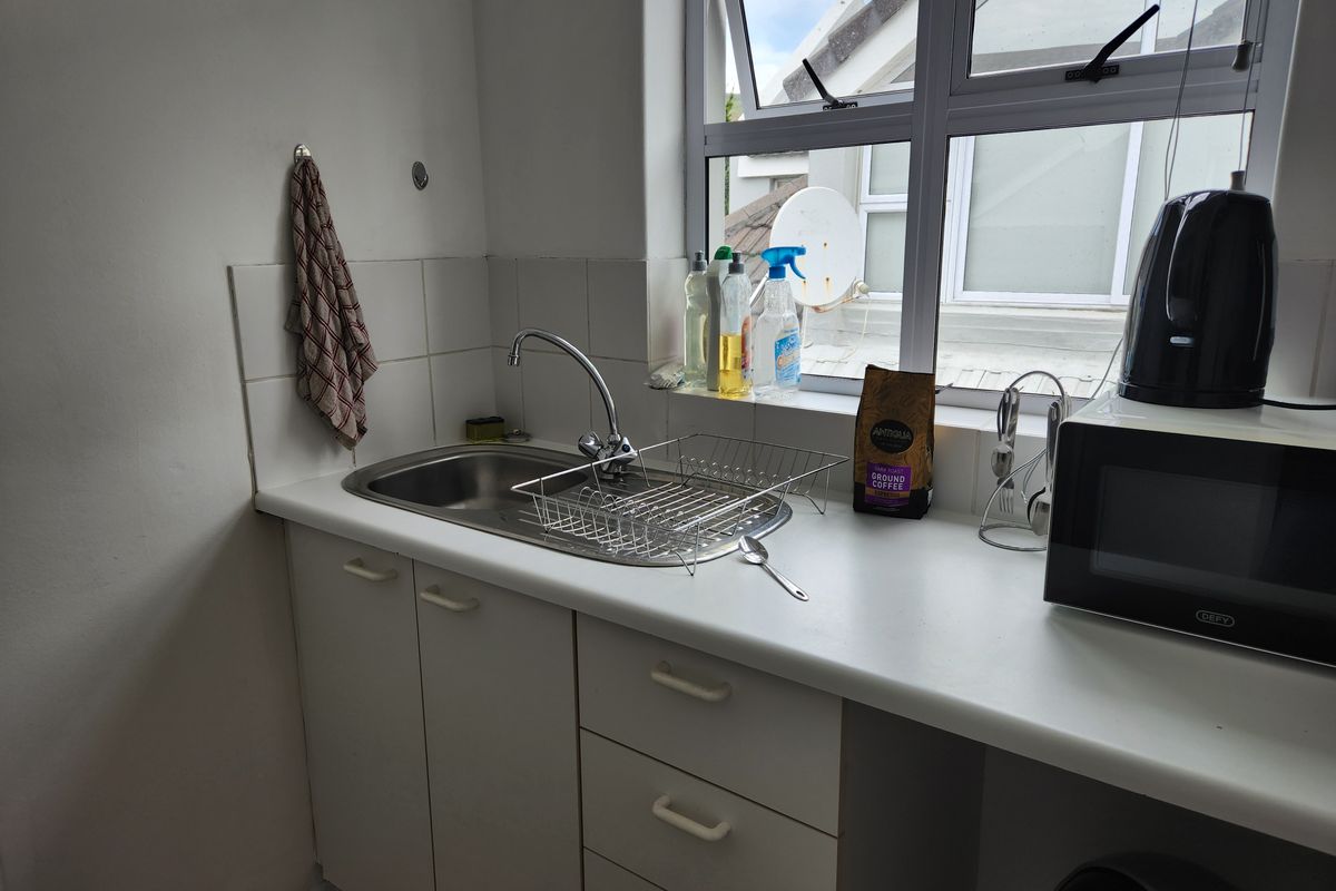 A compact kitchenette area featuring a stainless steel sink, white laminate countertops, and built-in cabinetry with a window providing natural light.