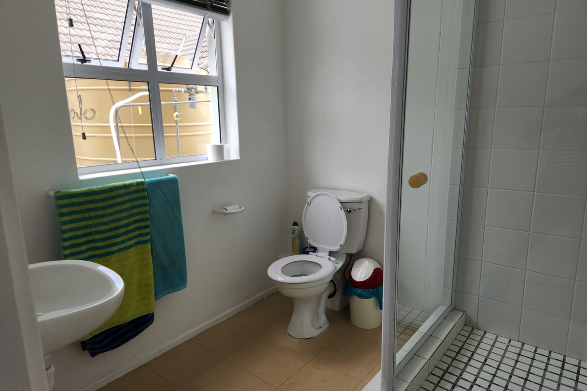 A functional office bathroom featuring a shower enclosure, wall-mounted basin, and toilet, with natural light provided by a window.