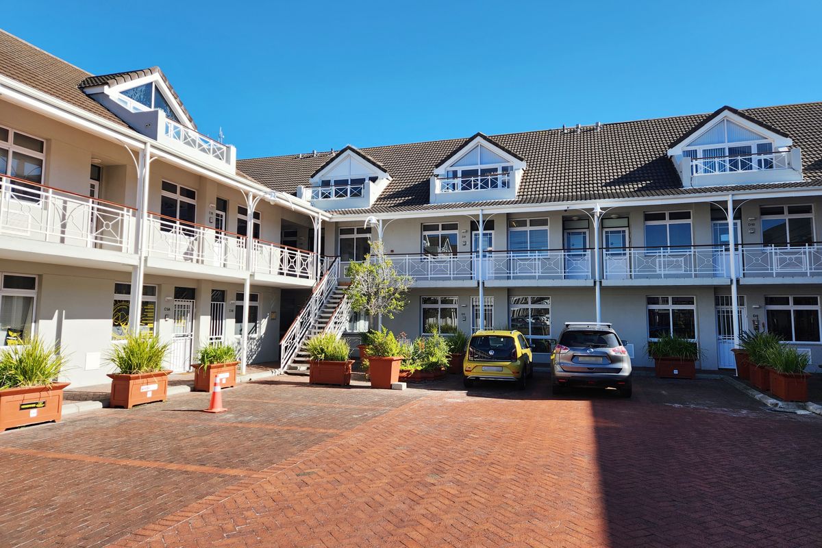A view of the office complex exterior featuring a paved courtyard, multi-level balconies with white railings, and tiled roofing.