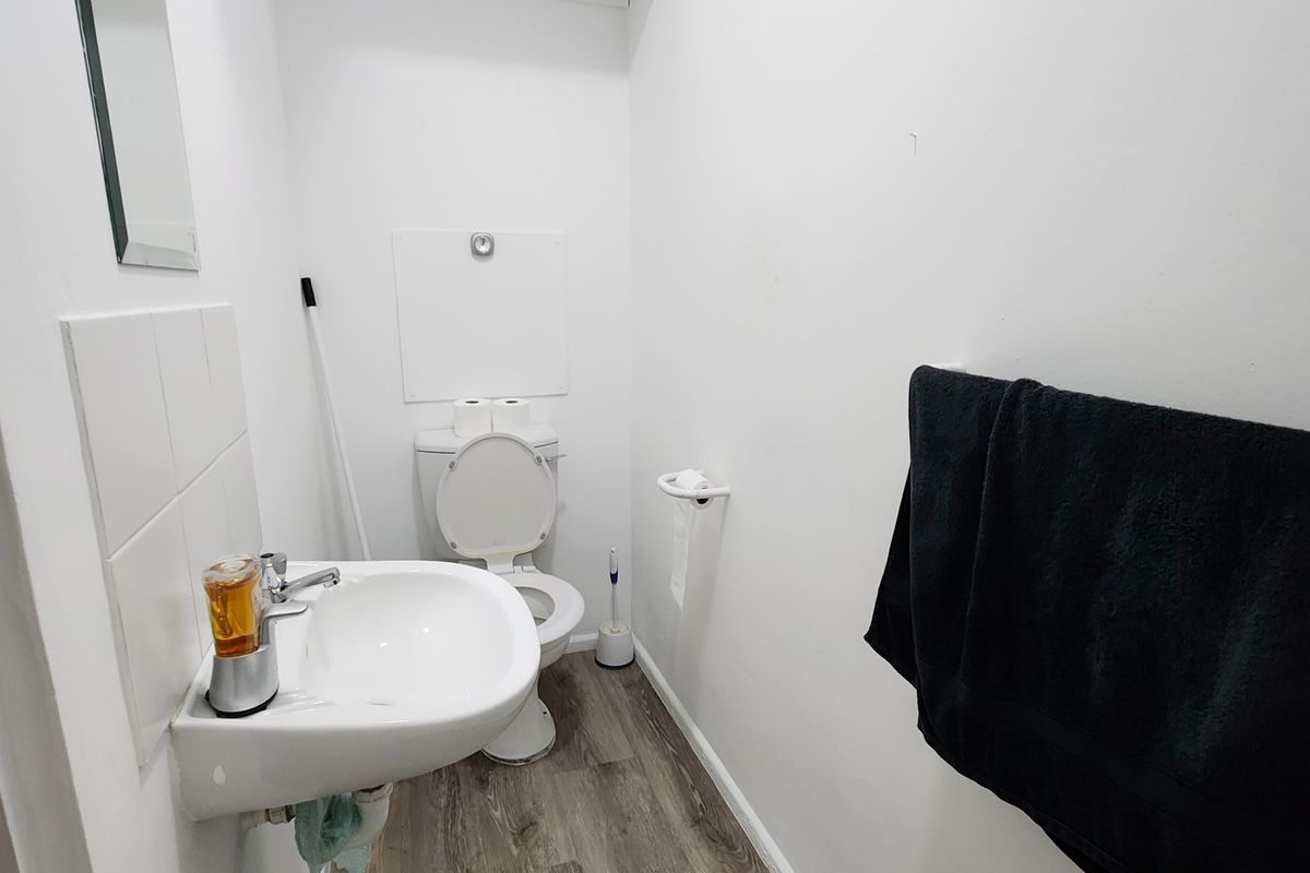 A compact office restroom featuring a wall-mounted basin, toilet, and wood-look vinyl flooring.