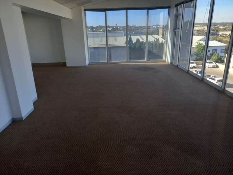 An empty, open-plan office space featuring large floor-to-ceiling windows that provide ample natural light and exterior views.