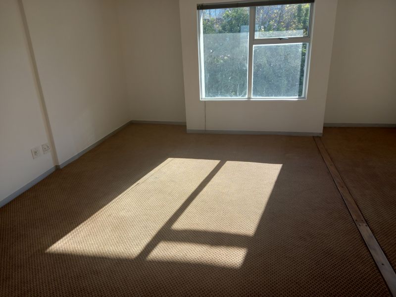 An empty office space featuring carpeted flooring, electrical outlets, and a window with blinds, providing a blank canvas for professional use.