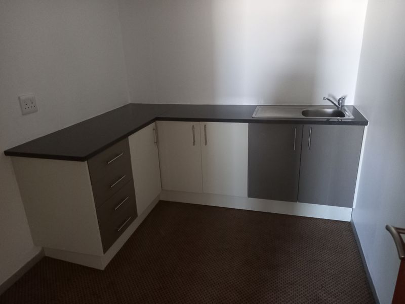 A compact office kitchenette featuring modern two-tone cabinetry, dark laminate countertops, and a stainless steel sink.