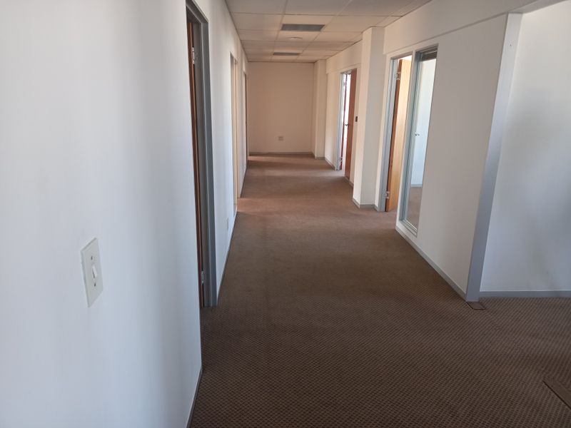 A long, empty office hallway featuring neutral carpeting, suspended ceilings, and multiple access points to individual office spaces.