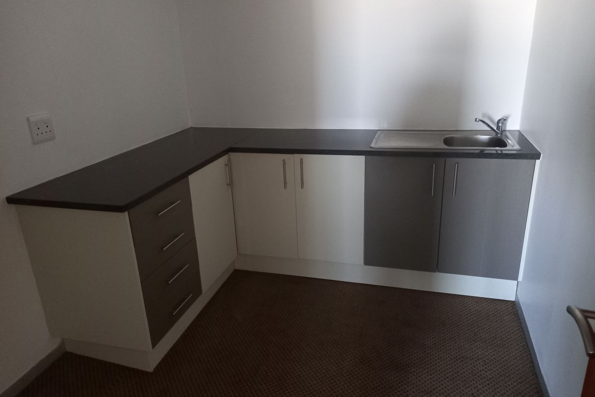 A compact office kitchenette featuring modern two-tone cabinetry, dark laminate countertops, and a stainless steel sink.
