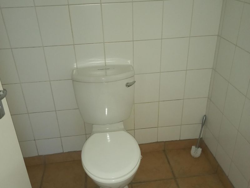 A functional office restroom featuring a standard toilet, white wall tiling, and terracotta-style floor tiles.