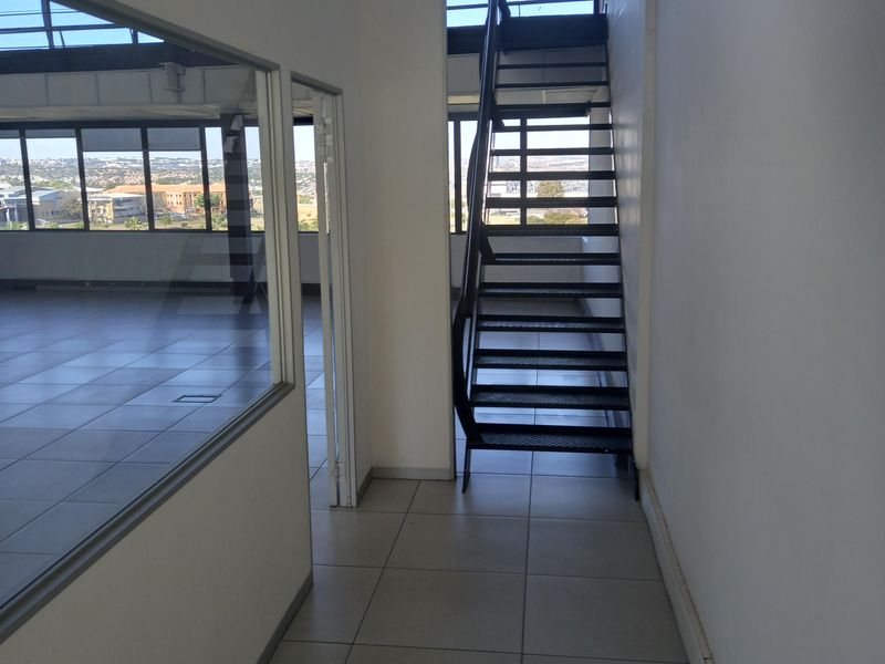 Modern office space featuring a sleek metal staircase, glass partitioning, and large windows offering expansive views, finished with neutral floor tiles.