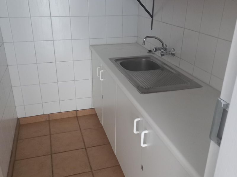 A compact scullery or kitchenette area featuring built-in cabinetry, a stainless steel sink, tiled splashback, and wall-mounted shelving.