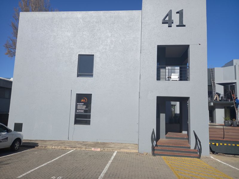 Front elevation of a modern two-story office building featuring a grey rendered facade, dedicated parking bays, and a prominent entrance staircase.