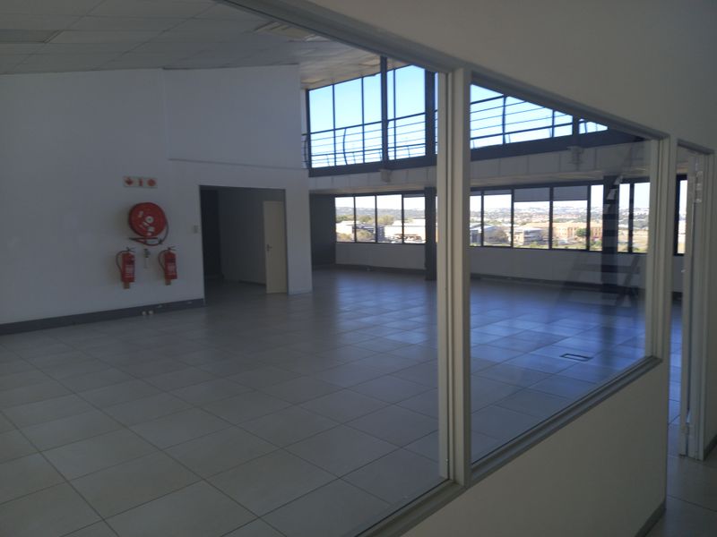 Spacious open-plan office area featuring large windows with natural light, tiled flooring, and integrated fire safety equipment.