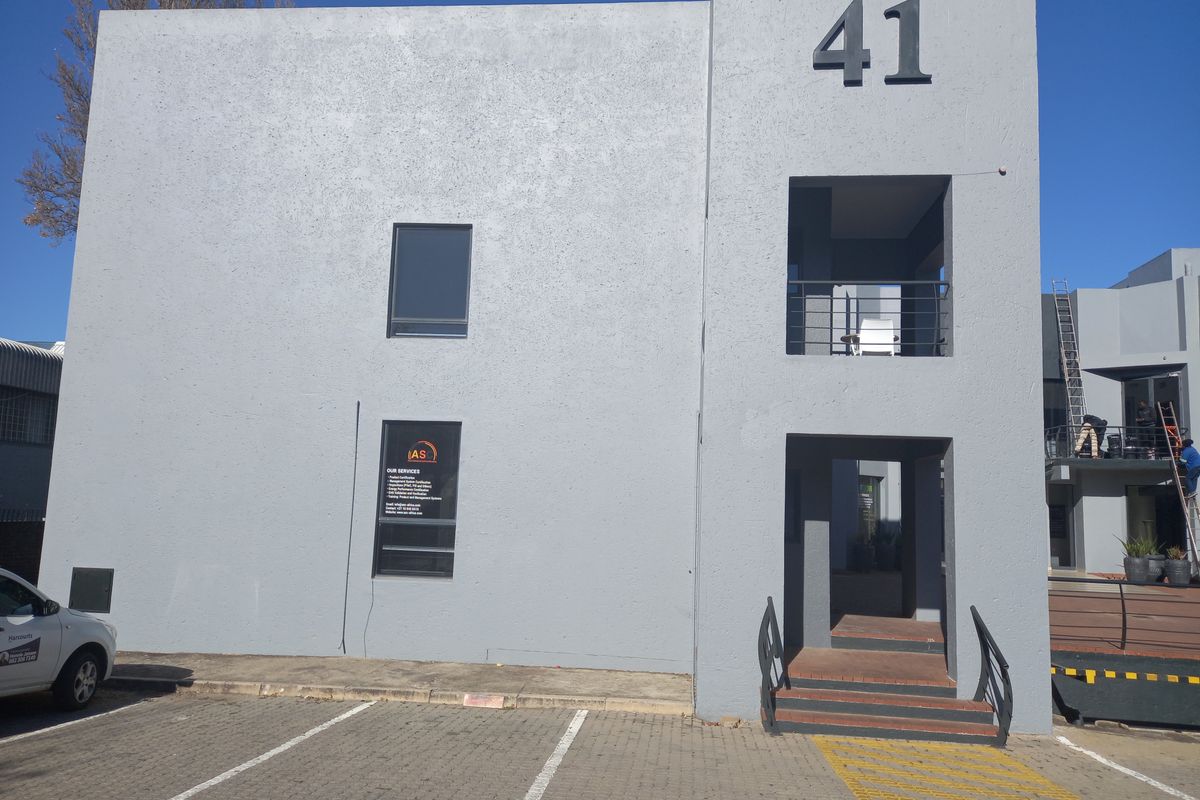 Front elevation of a modern two-story office building featuring a grey rendered facade, dedicated parking bays, and a prominent entrance staircase.