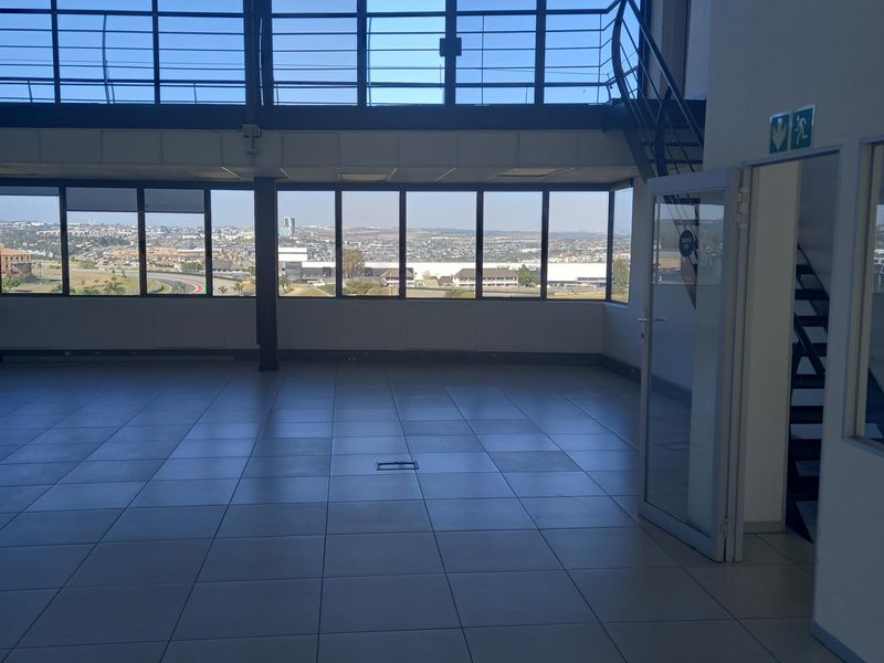 Spacious open-plan office area featuring a mezzanine level, large floor-to-ceiling windows with panoramic views, and modern tiled flooring.