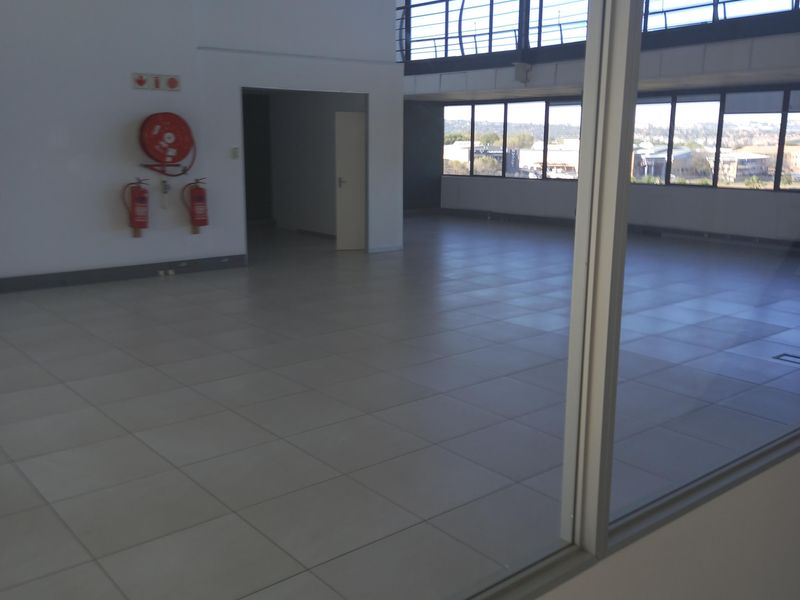A spacious, empty open-plan office area featuring large windows, tiled flooring, and integrated fire safety equipment, offering a bright and professional workspace.
