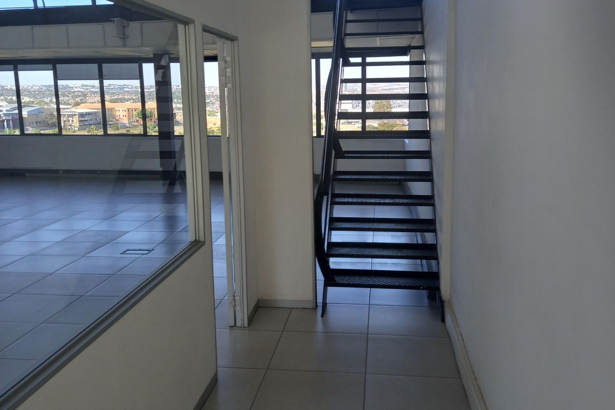 Modern office space featuring a sleek metal staircase, glass partitioning, and large windows offering expansive views, finished with neutral floor tiles.