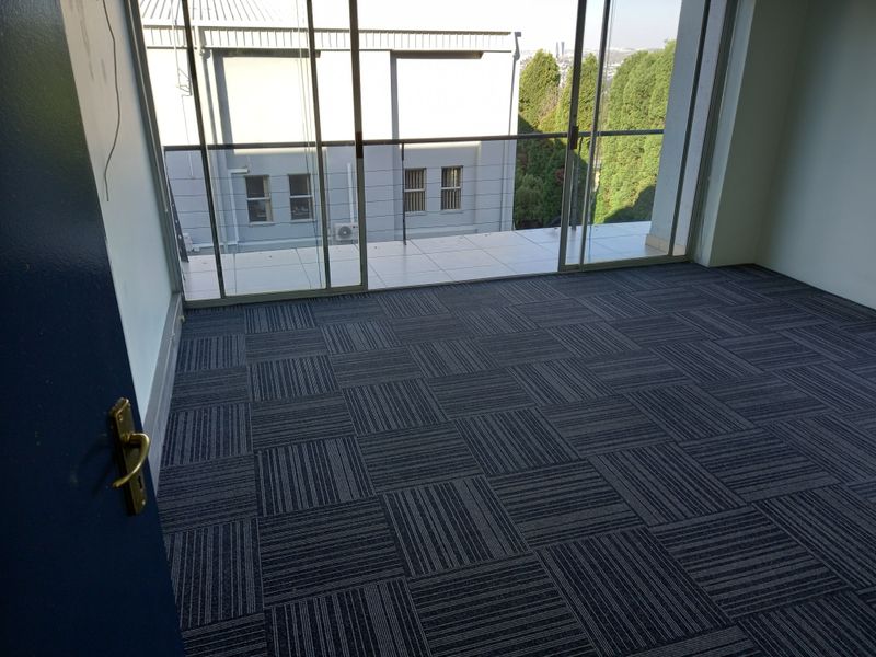 Empty office space featuring modern carpet tiles and large sliding glass doors leading to a private balcony with exterior views.