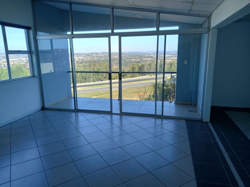Empty office space featuring large aluminium sliding doors, tiled flooring, and expansive views of the surrounding landscape.